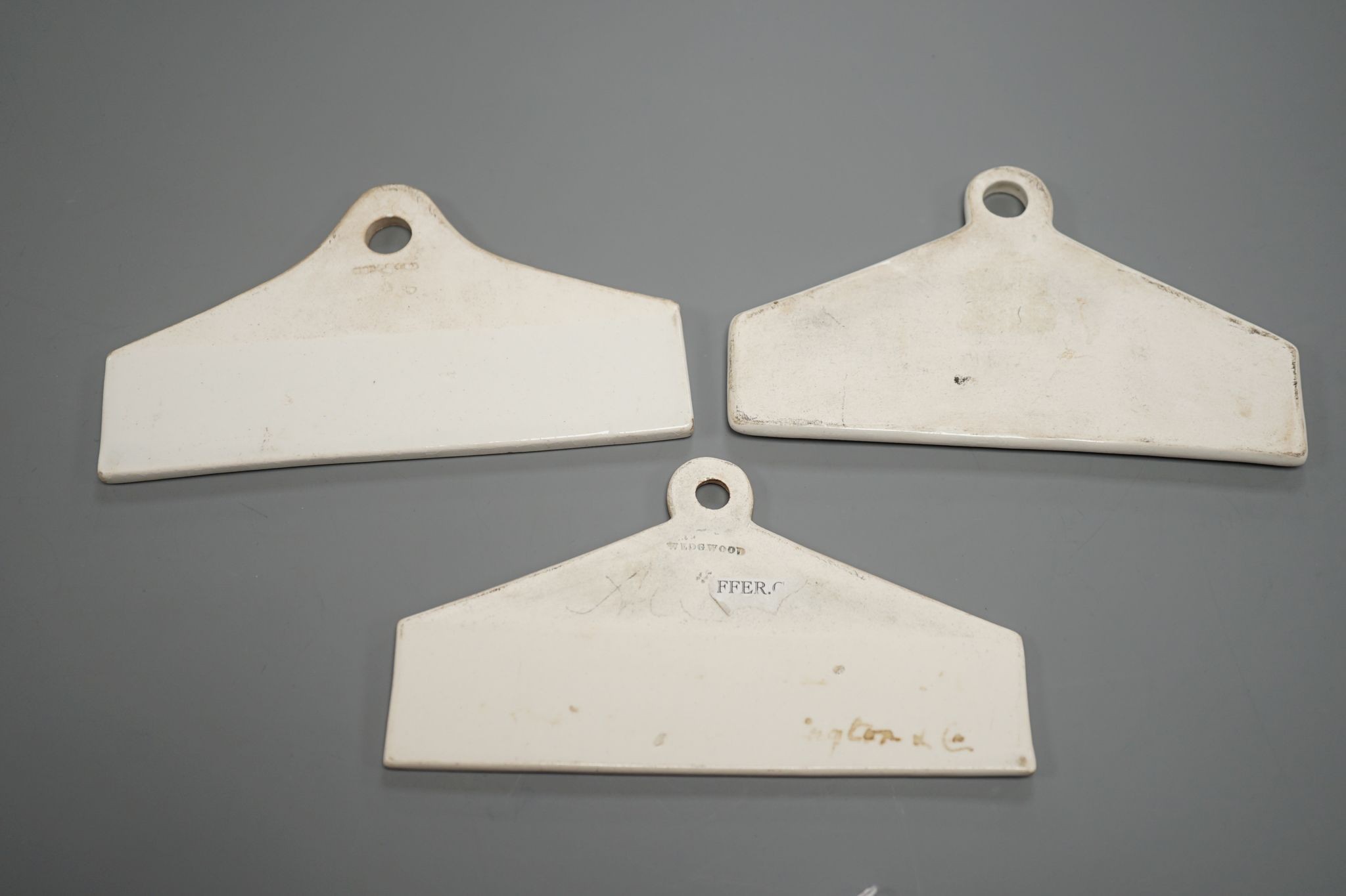 Three late 18th century creamware cellar labels, two claret stamped Wedgwood and one sherry, unmarked, 14 cms wide.